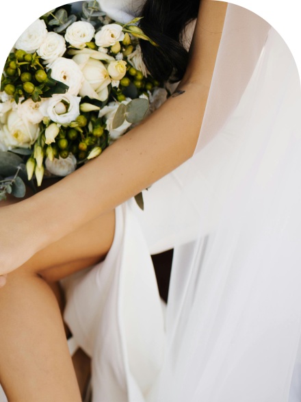 Close-up of a floral necklace adorning a bride in a strapless white wedding dress outdoors.