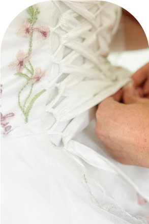 Delicate hands tying the back of a floral wedding dress, symbolizing care and elegance.